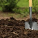 Shovel in soil outdoors, space for text. Gardening tool